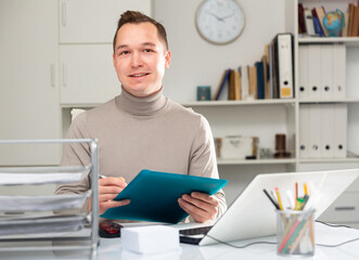 Caucaisan businessman doing his daily work in office. Cheerful man sitting at desk and looking at...