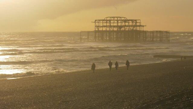 Brighton west pier ruin in evening light, people walking on beach