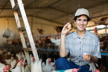 Successful young hispanic woman farmer working breeding laying hens, showing freshly picked organic...