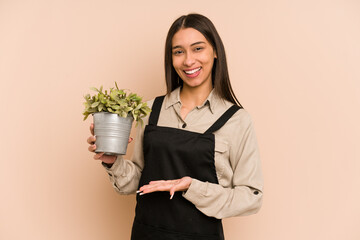 Young colombian gardener woman holding a plant isolated showing a copy space on a palm and holding...