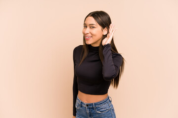 Young colombian woman isolated on beige background trying to listening a gossip.