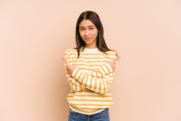 Young colombian woman isolated on beige background points sideways, is trying to choose between two...