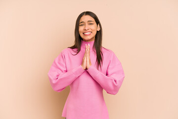 Obraz premium Young colombian woman isolated on beige background holding hands in pray near mouth, feels confident.