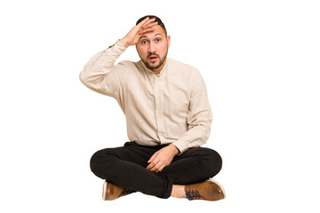 Adult latin man sitting on the floor cut out isolated shouts loud, keeps eyes opened and hands tense.