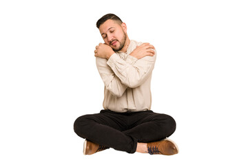 Adult latin man sitting on the floor cut out isolated hugs, smiling carefree and happy.