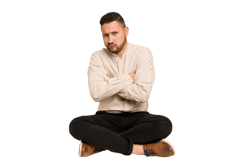 Adult latin man sitting on the floor cut out isolated frowning face in displeasure, keeps arms folded.