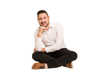Adult latin man sitting on the floor cut out isolated smiling happy and confident, touching chin...