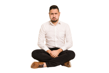 Adult latin man sitting on the floor cut out isolated blows cheeks, has tired expression. Facial expression concept.