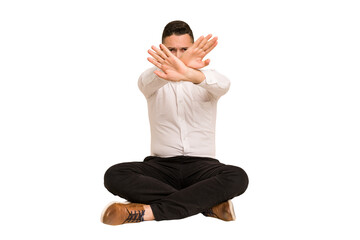 Adult latin man sitting on the floor cut out isolated doing a denial gesture