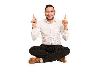 Adult latin man sitting on the floor cut out isolated indicates with both fore fingers up showing a...