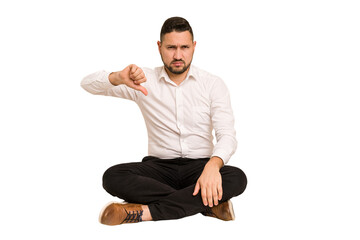 Adult latin man sitting on the floor cut out isolated showing thumb down, disappointment concept.