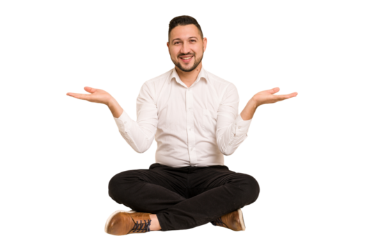 Adult latin man sitting on the floor cut out isolated makes scale with arms, feels happy and confident.
