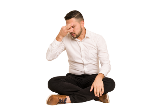 Adult latin man sitting on the floor cut out isolated having a head ache, touching front of the face.