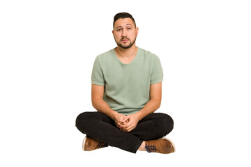 Adult latin man sitting on the floor cut out isolated sad, serious face, feeling miserable and...