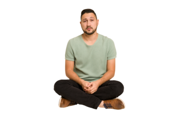 Adult latin man sitting on the floor cut out isolated sad, serious face, feeling miserable and displeased.