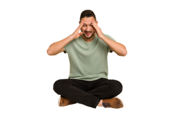Adult latin man sitting on the floor cut out isolated touching temples and having headache.