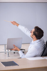 Young male teacher sitting in the classroom