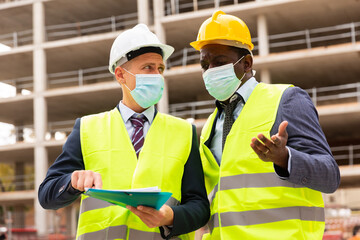 Portrait of an engineer and architect in protective mask with folder of documents at a construction site