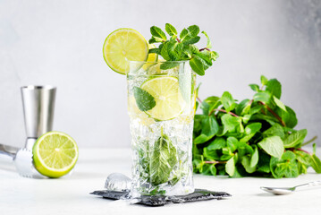 Mojito classic summer alcoholic cocktail with lime, white rum, soda, cane sugar, mint, and ice in highball glass on gray background. Copy space