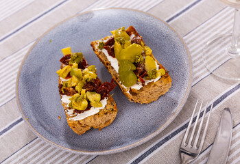 Healthy sandwiches for breakfast or lunch with toasted baguette, cream cheese spread, slices of sun-dried tomatoes, green olives and pesto. Mediterranean style vegetarian appetizers