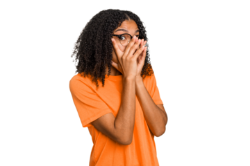 Young african american woman with curly hair cut out isolated blink through fingers frightened and nervous.