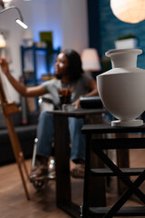 Female art student living with medical condition drawing vase pencil sketch on canvas. Close up of ceramic sculpture with african american artist in background making artwork.