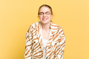 Young caucasian redhead woman isolated on yellow background laughs and closes eyes, feels relaxed and happy.