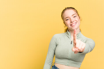 Young caucasian redhead woman isolated on yellow background showing number one with finger.