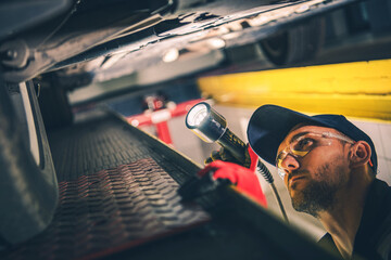 Mechanic Checking Car Undercarriage During Regular Vehicle Inspection - obrazy, fototapety, plakaty