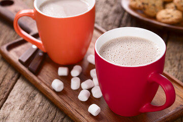 Hot cocoa or hot chocolate in cups with marshmallows on the side and cookies in the back, photographed on wood (Selective Focus, Focus in the middle of the right cocoa's surface)