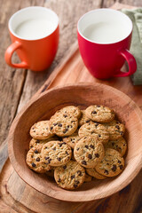 Chocolate chip cookies in wooden bowl with two cups of milk in the back, photographed on wood (Selective Focus, Focus one third into the bowl)
