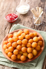 Fresh round baked Duchess potatoes or croquettes on wooden plate, ketchup, mayonnaise and food picks in the back (Selective Focus, Focus one third into the potato balls)