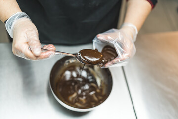 Top view a expert putting chocolate icing into a pastry bag form a metal bowl with a spoon. High quality photo