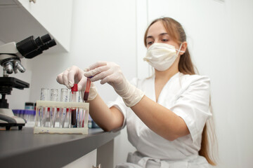 girl doctor in uniform and a medical mask holds test tubes with blood tests in the laboratory