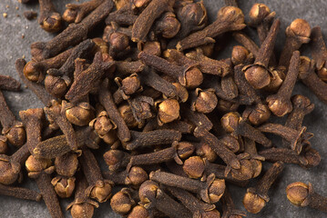 Brown dried cloves, textured on a gray stone background.