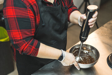 Side view of a baker blending chocolate icing in a metal bowl. High quality photo