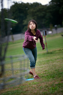 A young Asian-American woman plays flying disk golf in Baltimore, Maryland.