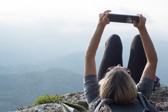 Mature woman hiker reclines on cliff edge with ipad