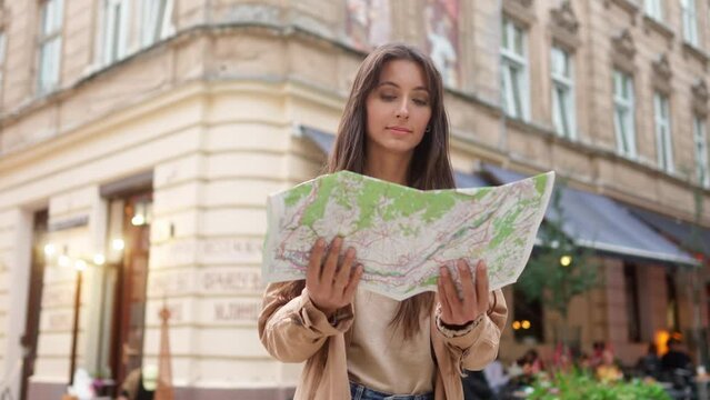 Portrait of young beautiful adventurous woman traveling standing in city center of Lviv holding map. Attractive happy female tourist looking at camera smiling planning routes for sightseeing.