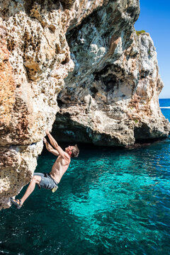 A Young Man Climbs On Rock At Mediterranean Sea In Cala Varques, Spain