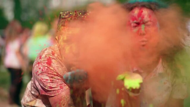 Joyful guy and girl blowing paints into the lens at the festival of colors Holi