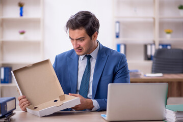 Young male employee eating pizza at workplace