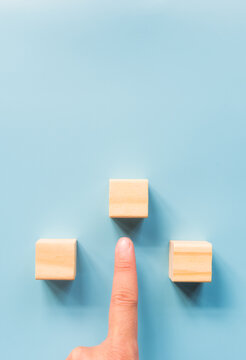 human finger pointing to One of three wooden cubes. view from the top and space for text