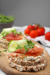 Crunchy buckwheat cakes with cream cheese, prosciutto and cucumber slices on wooden board, closeup