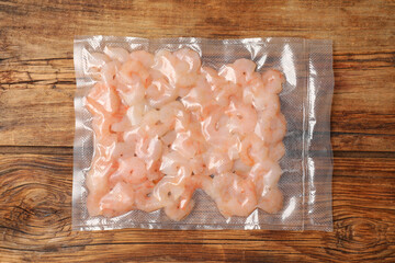 Vacuum pack of shrimps on wooden table, top view