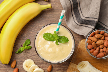 Flat lay composition of banana smoothie in glass and nuts on wooden table