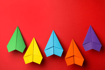 Handmade colorful paper planes on red background, flat lay. Space for text