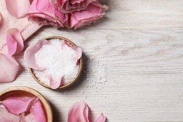 Flat lay composition with sea salt and beautiful petals of roses on white wooden table, space for text