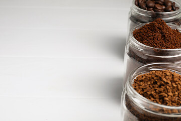 Jars with instant, ground coffee and roasted beans on white table, space for text