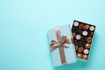 Open box of delicious chocolate candies on light blue background, flat lay. Space for text